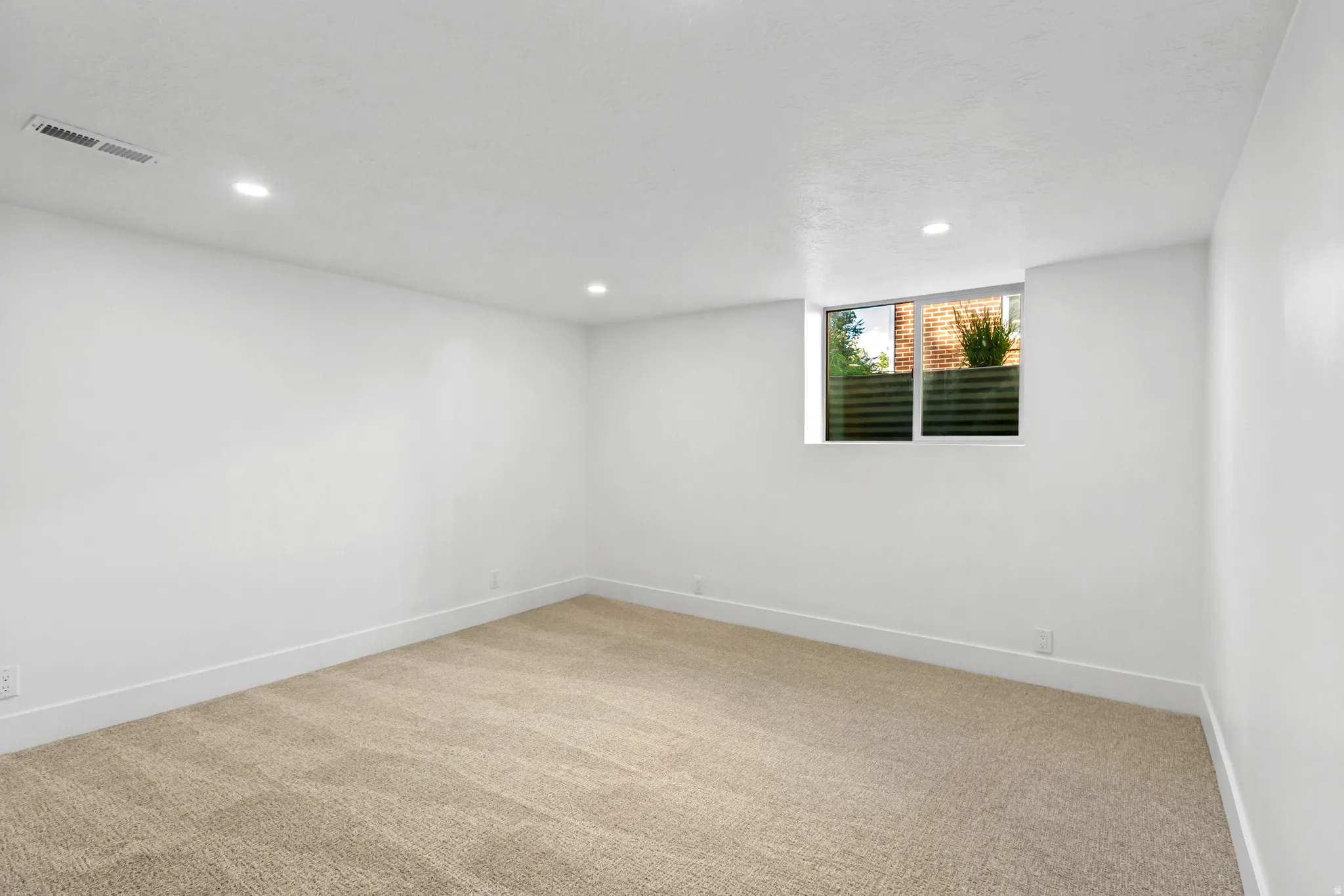 Recessed lighting, neutral-toned carpet, white walls, white trim, and a window with exterior brick detail