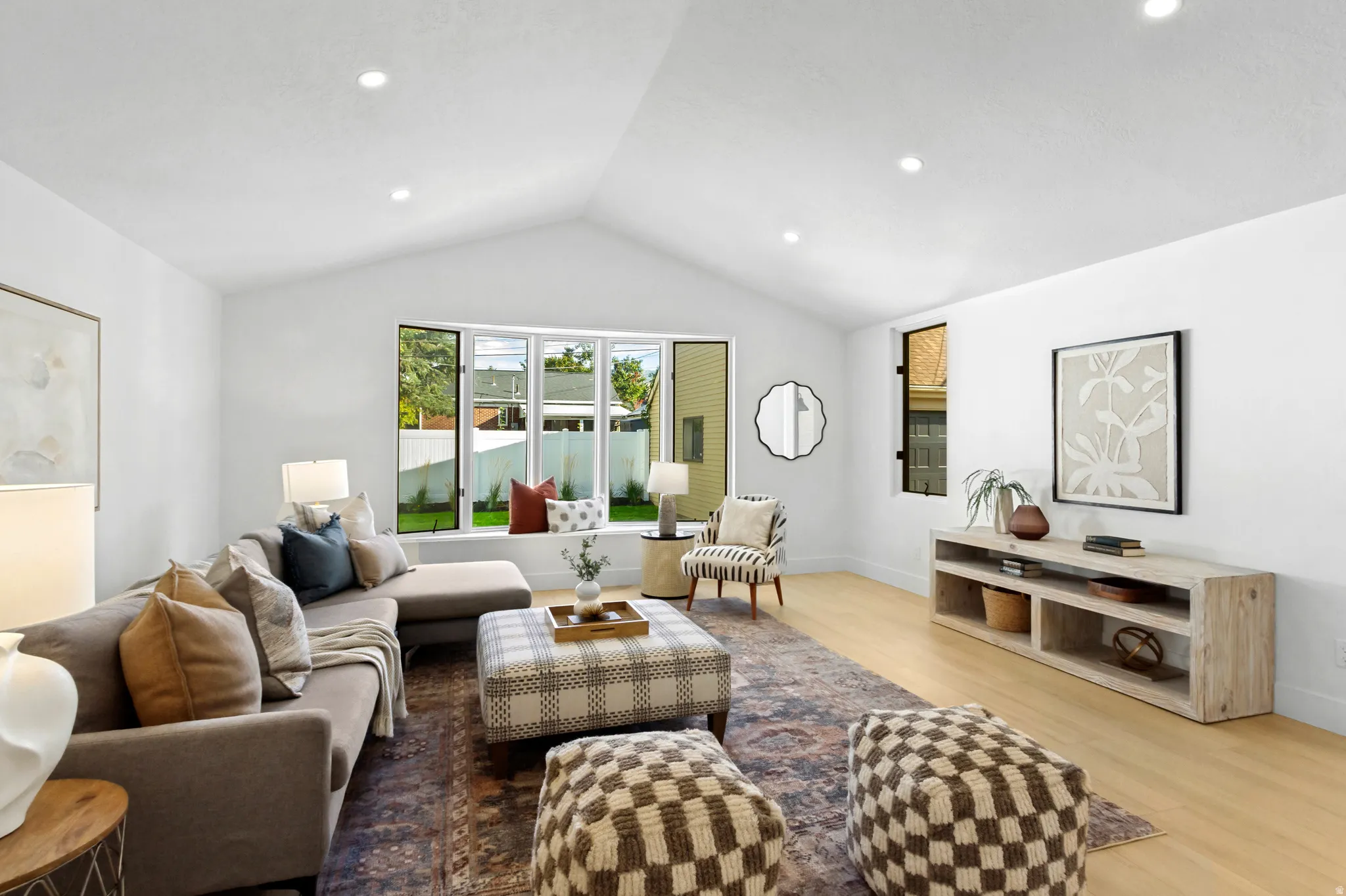 Vaulted ceiling with recessed lighting, large bay window, light wood-finish flooring, and a built-in media console