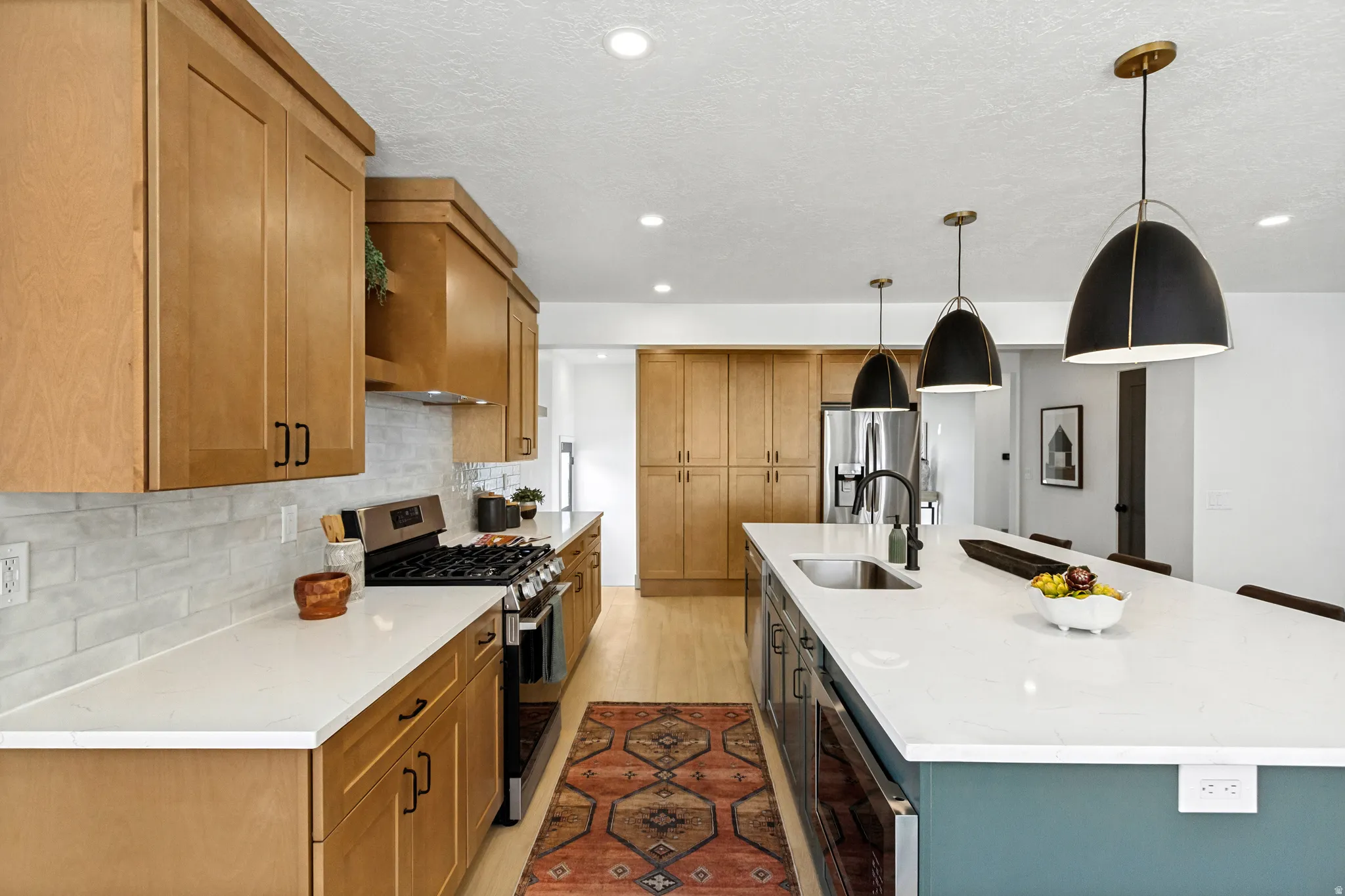 Kitchen featuring light wood cabinetry, white countertops, stainless steel appliances, and an expansive island with a built-in sink
