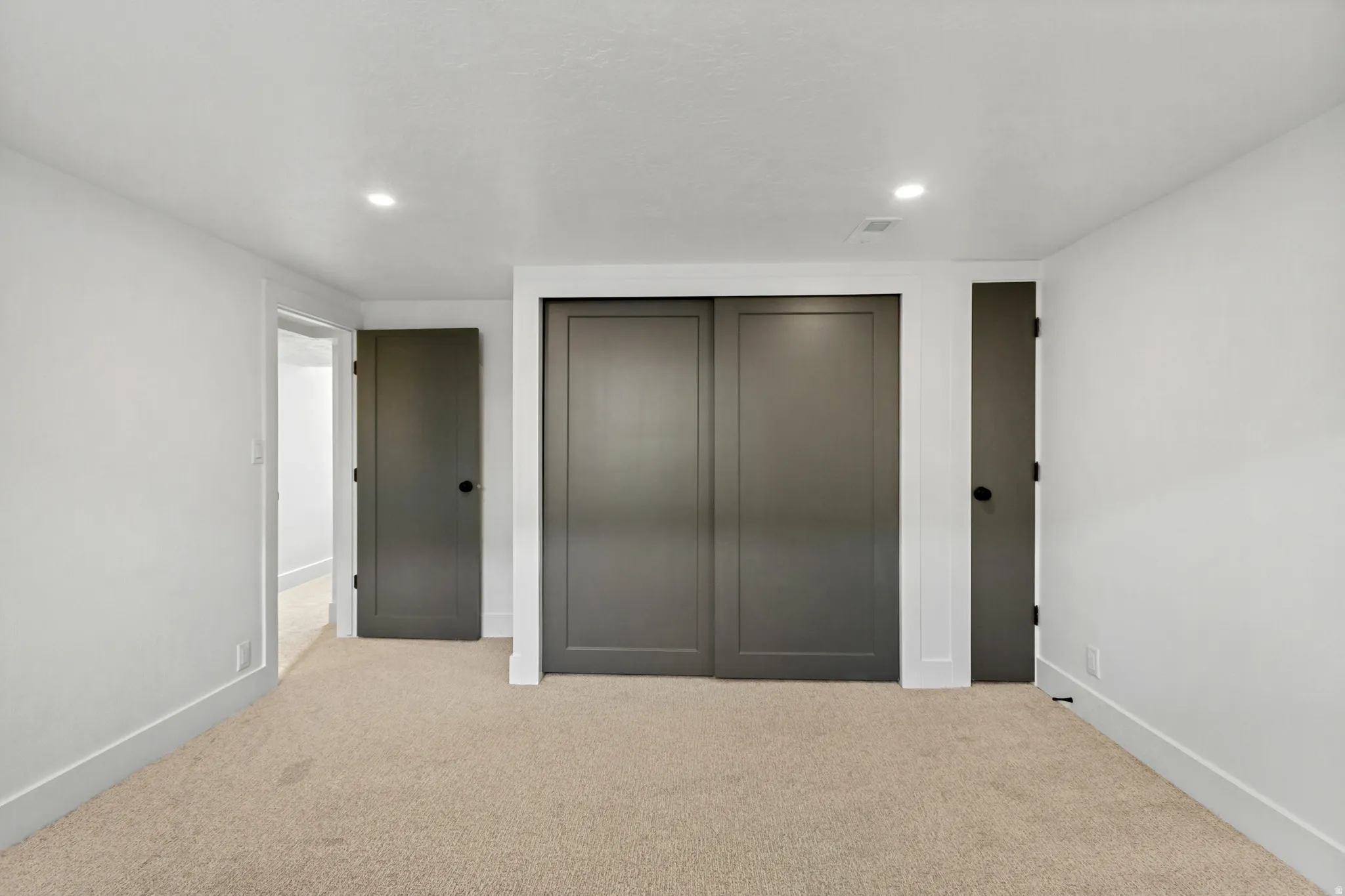 Recessed lighting, neutral carpeting, and white walls