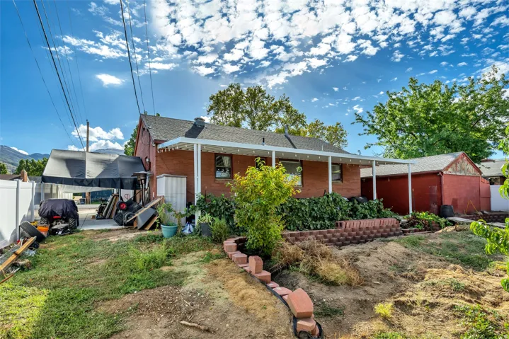 Brick exterior with covered patio, white vinyl fencing, and detached storage structure