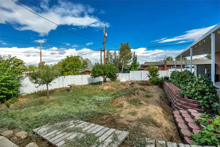 Expansive outdoor area featuring a retaining wall, mature trees, and a white privacy fence