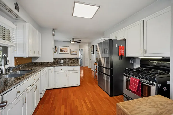 Kitchen with wood-finish flooring, white cabinetry, granite-style countertops, and stainless steel appliances
