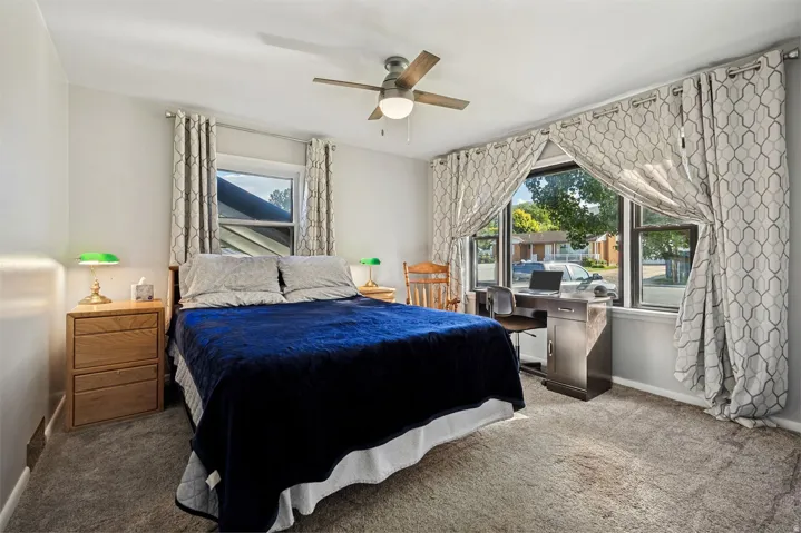 Carpeted room with a ceiling fan, two windows with blinds, and a large window with drapes