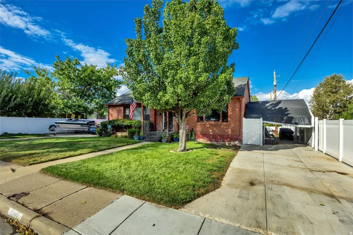 Brick exterior with mature tree and lawn, featuring a covered carport and a fenced side yard