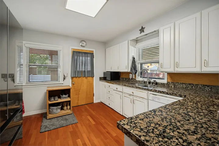 Kitchen featuring wood-finish flooring, white cabinetry, a stainless steel sink, and granite-style countertops