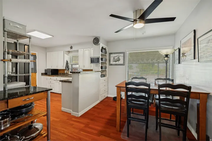 Kitchen and dining area featuring wood-finish flooring, white cabinetry, dark stone countertops, and a ceiling fan with integrated lighting