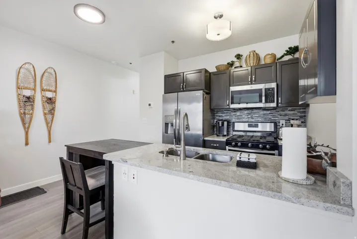 Kitchen featuring granite countertops, stainless steel appliances, dark wood-finish cabinetry, a tiled backsplash, and wood-finish flooring