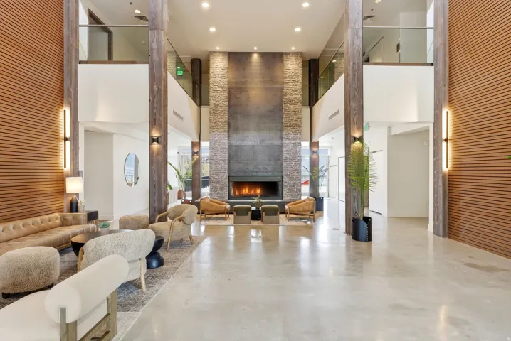 Two-story lobby featuring concrete flooring, a fireplace with a stone surround, wood-finish wall paneling, and glass railings on the upper level