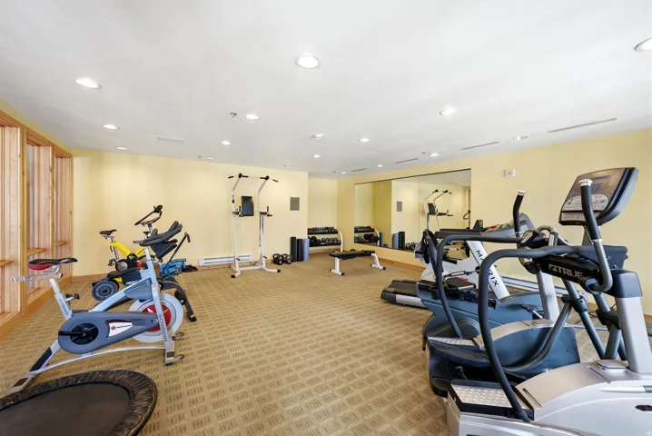 Fitness area with patterned carpet flooring, recessed lighting, and mirrored wall