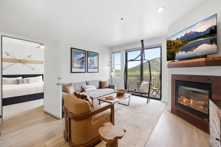 Recessed lighting, wood-finish flooring, a contemporary fireplace with a wood mantle, and a sliding glass door to an outdoor balcony