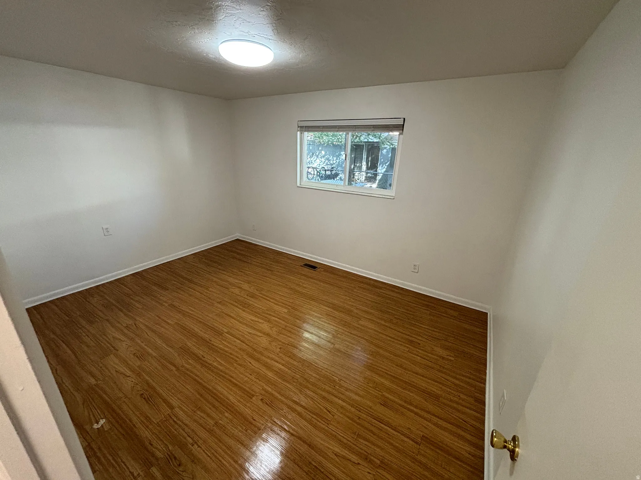 Wood-finish flooring, white walls, single window, and flush-mount ceiling light