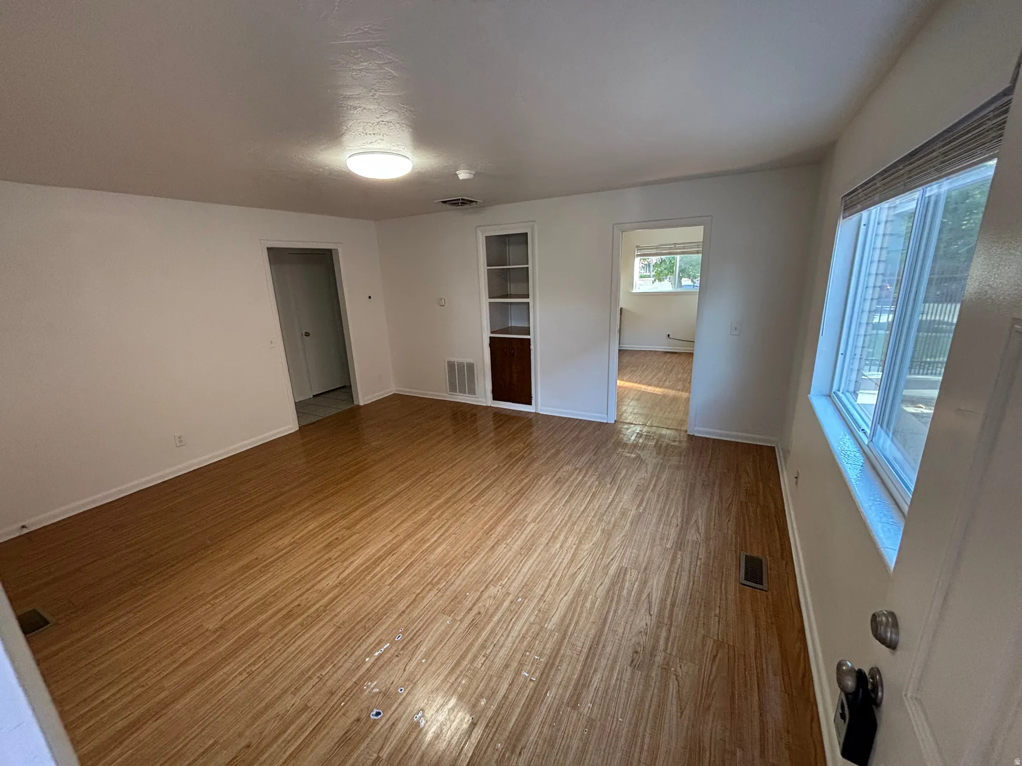 Wood-finish flooring throughout, white walls, built-in shelving, and a prominent window with horizontal blinds