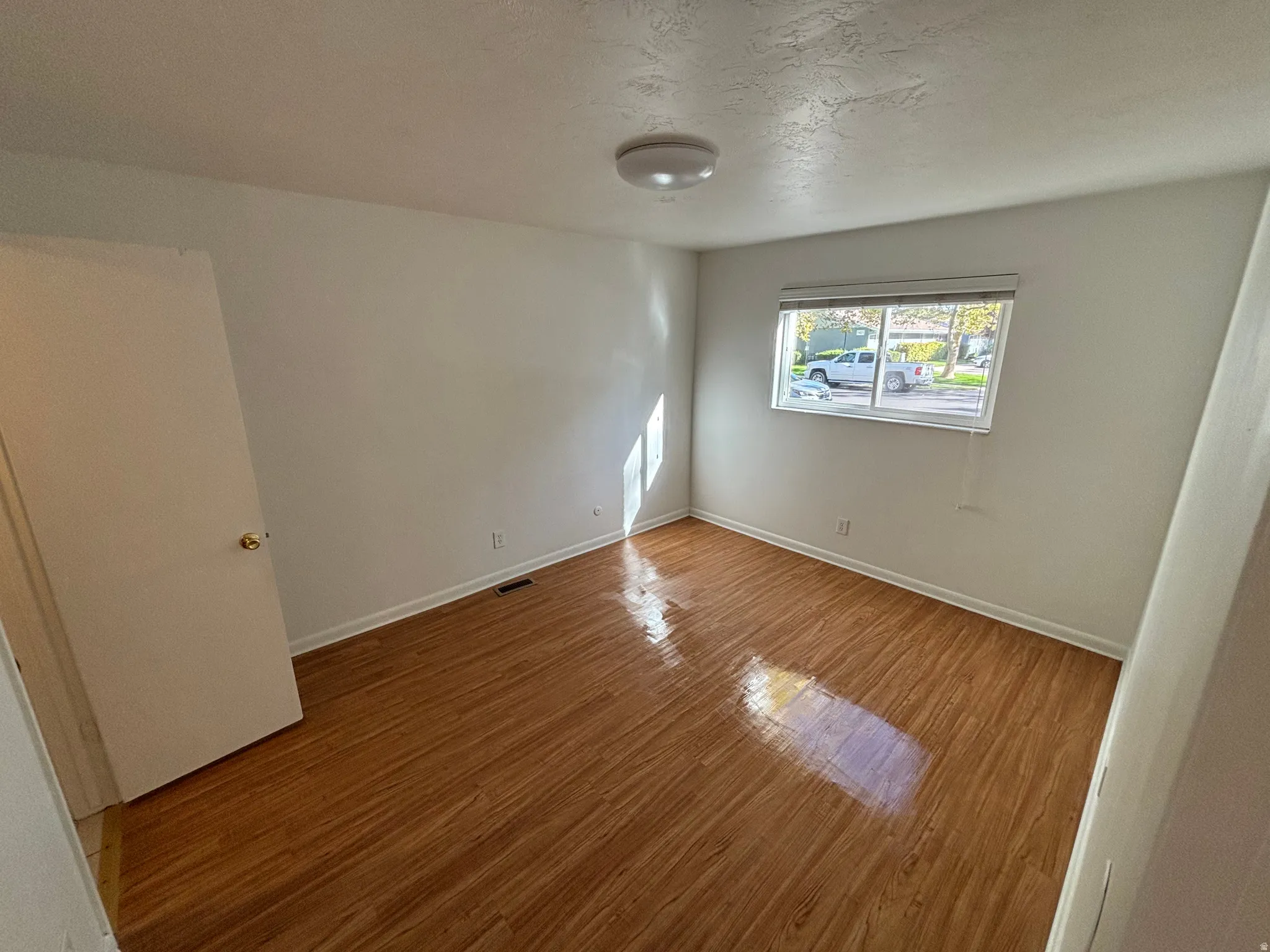 Neutral wall color, wood-finish flooring, and a single window with blinds