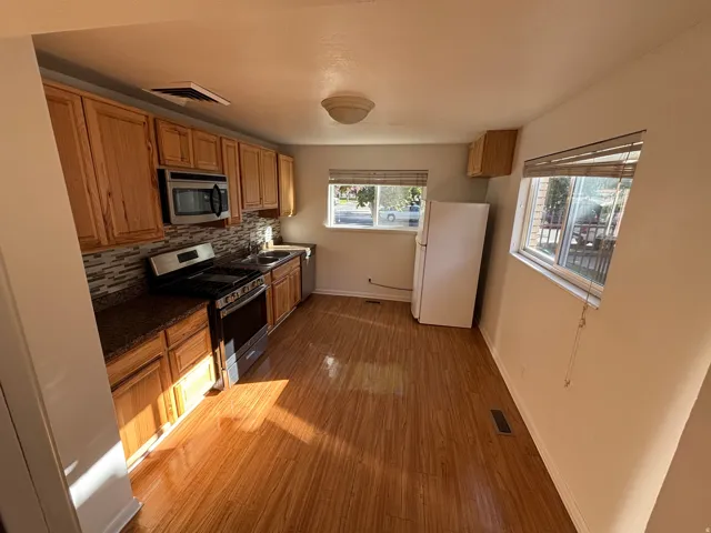 Kitchen featuring wood-finish cabinetry, stainless steel appliances, mosaic tile backsplash, and light wood-finish flooring