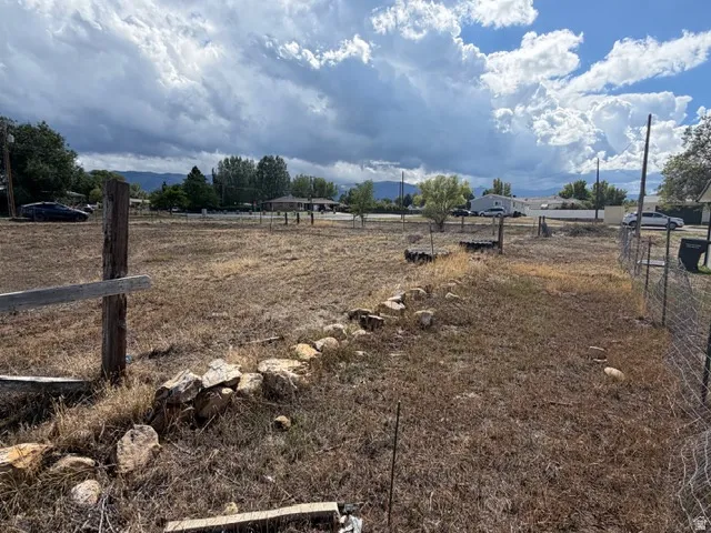 Expansive lot featuring a partial wire fence, rock border, and mature trees in the background