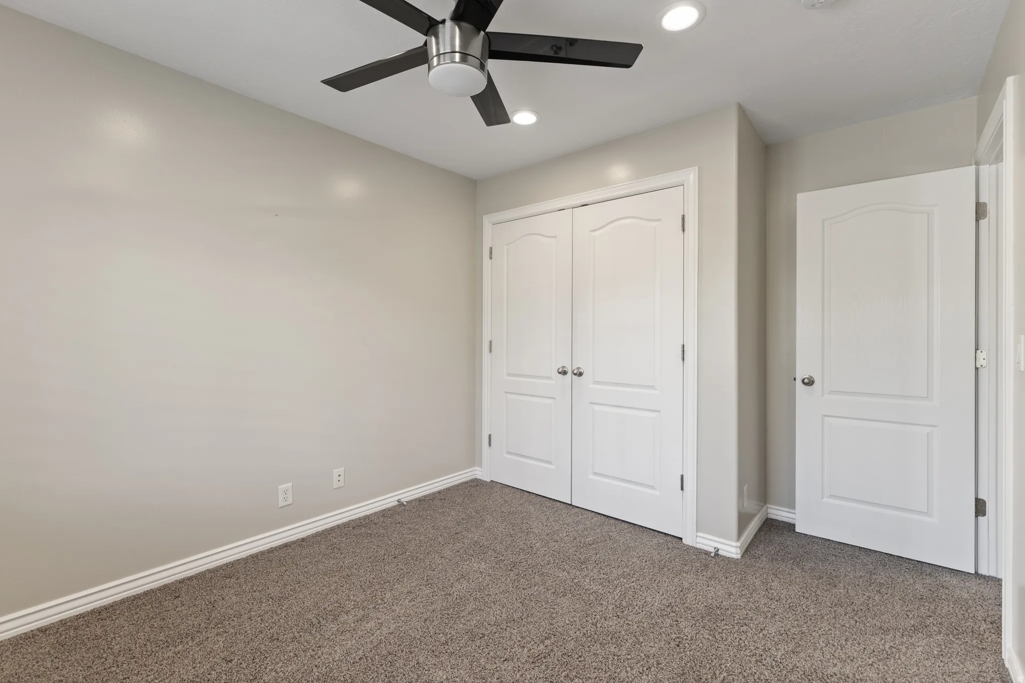 Plush carpeted flooring, two paneled closet doors, a paneled interior door, ceiling fan with integrated lighting, and recessed ceiling lights