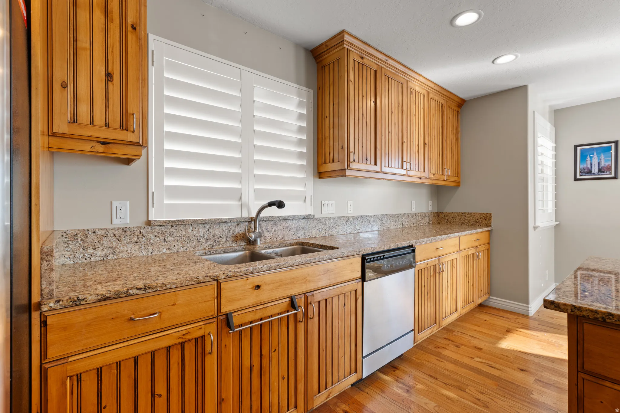 Wood-finish cabinetry, granite countertops, stainless steel dishwasher, double basin sink, and wood-finish flooring