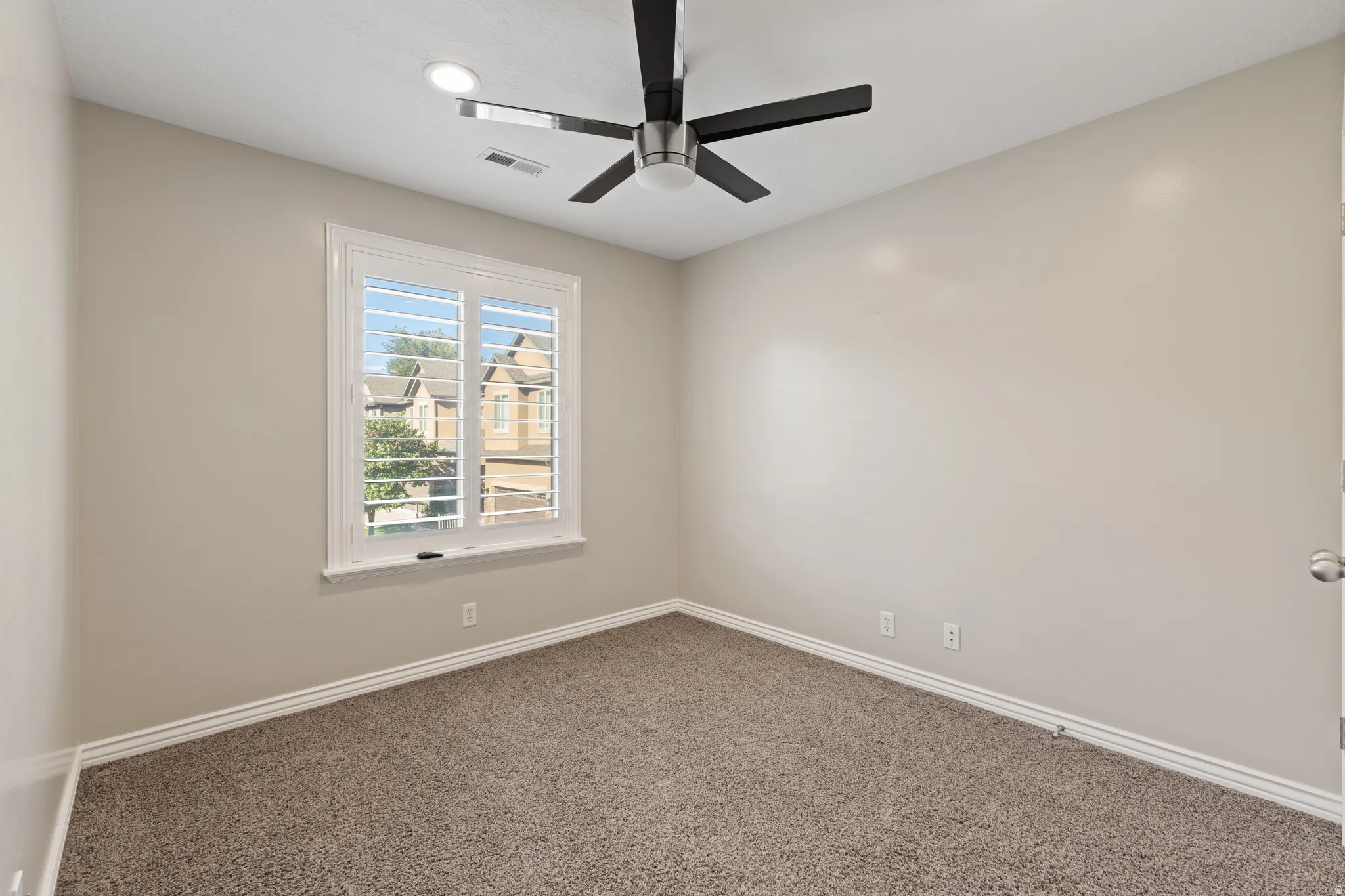 Recessed lighting, ceiling fan, neutral wall paint, white window frame with plantation shutters, and carpet flooring
