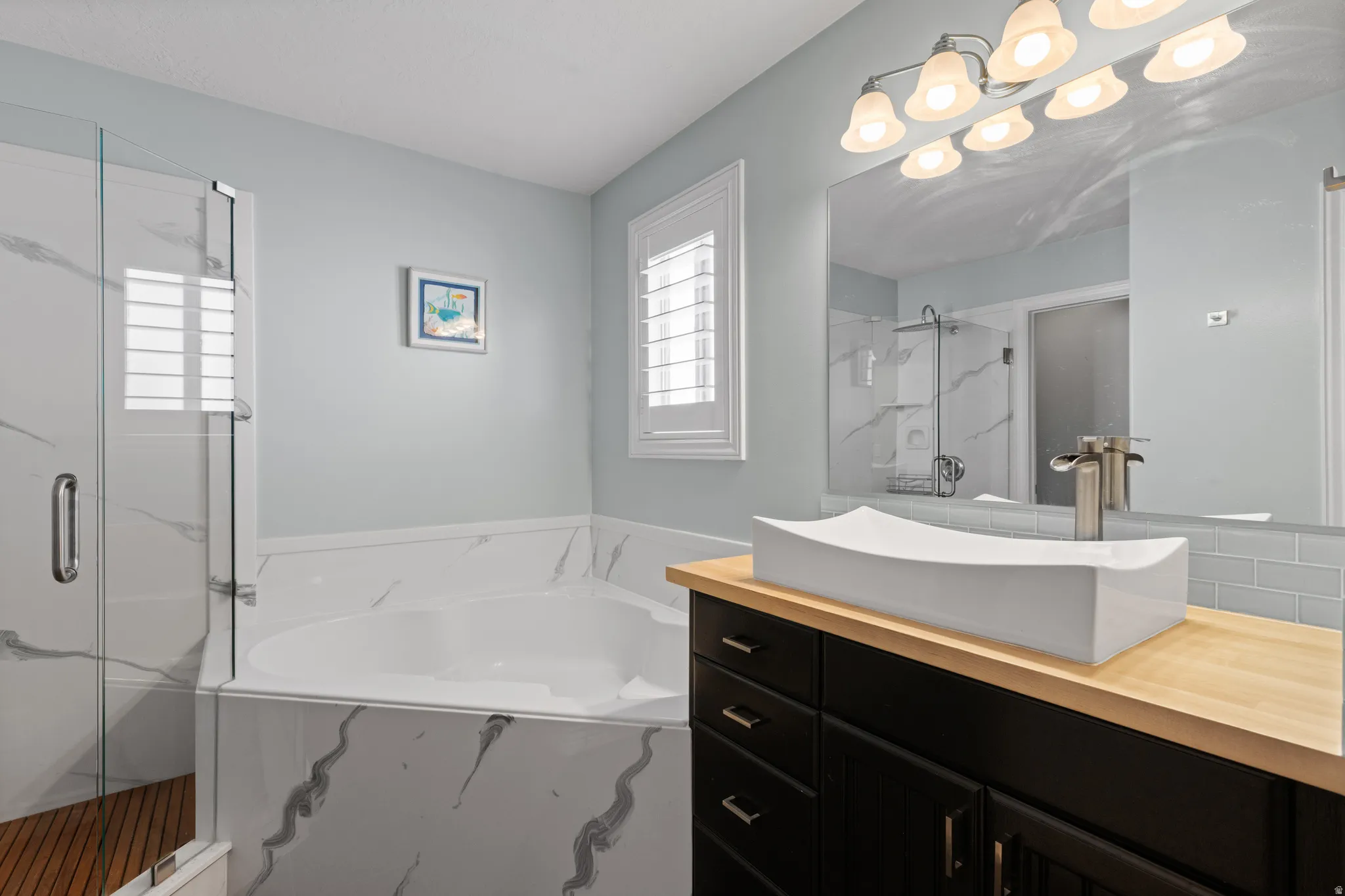 Bathroom featuring a corner soaking tub, glass-enclosed shower with wood-finish flooring, dark wood vanity with a light wood-finish countertop, and a vessel sink