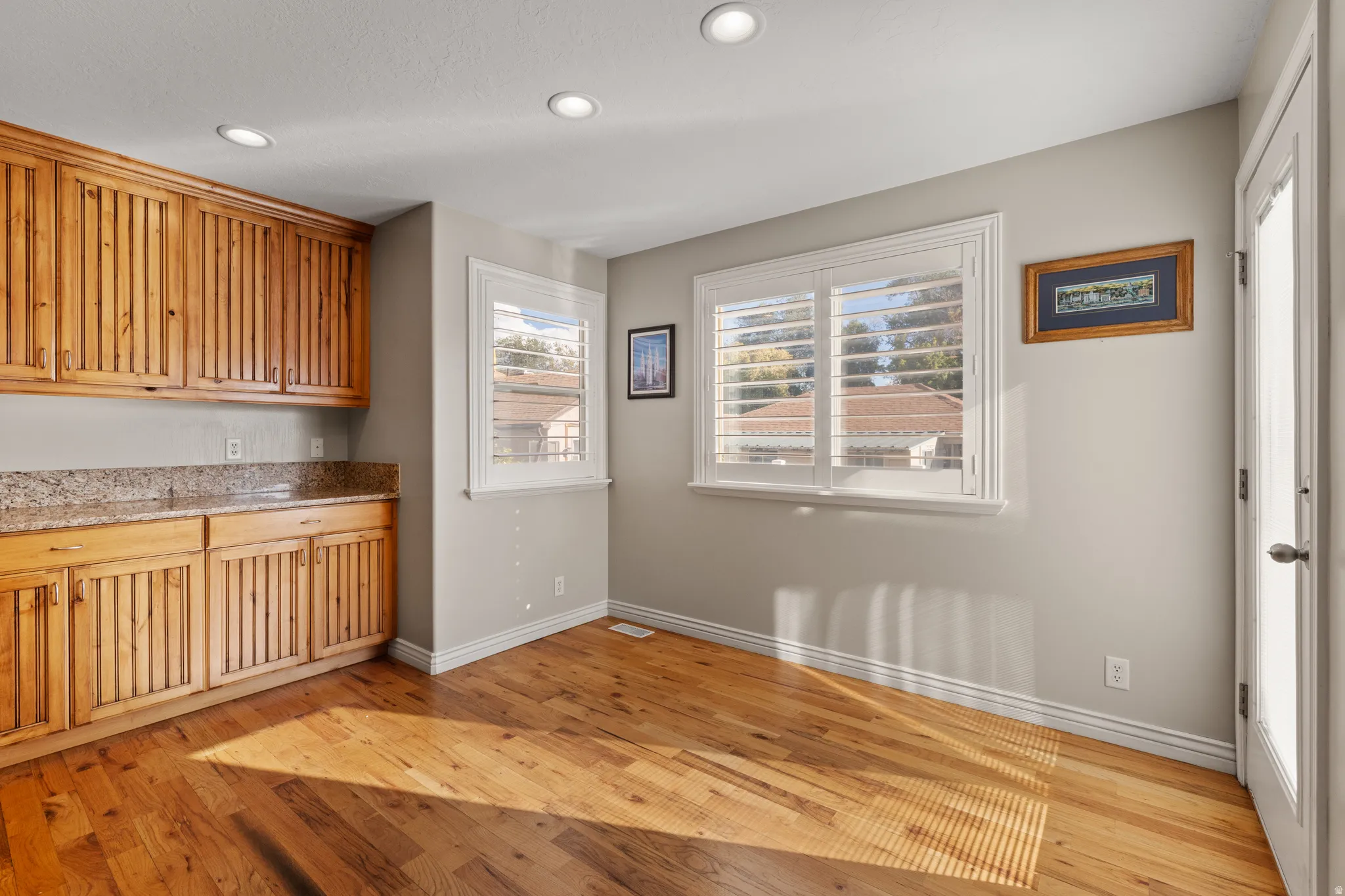 Wood-finish flooring, built-in wooden cabinetry, stone counter, recessed lighting, and windows with plantation shutters