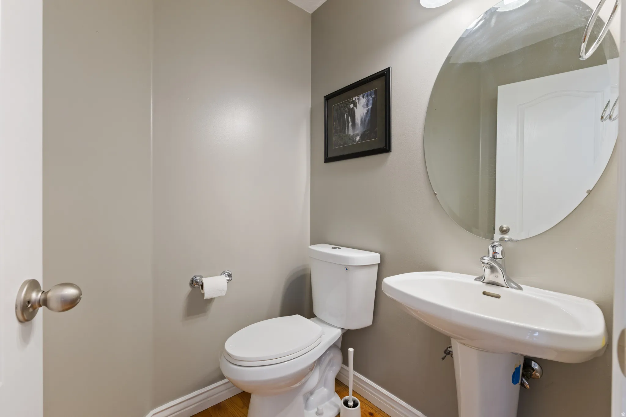 Pedestal sink with chrome faucet, oval wall mirror, and neutral wall color