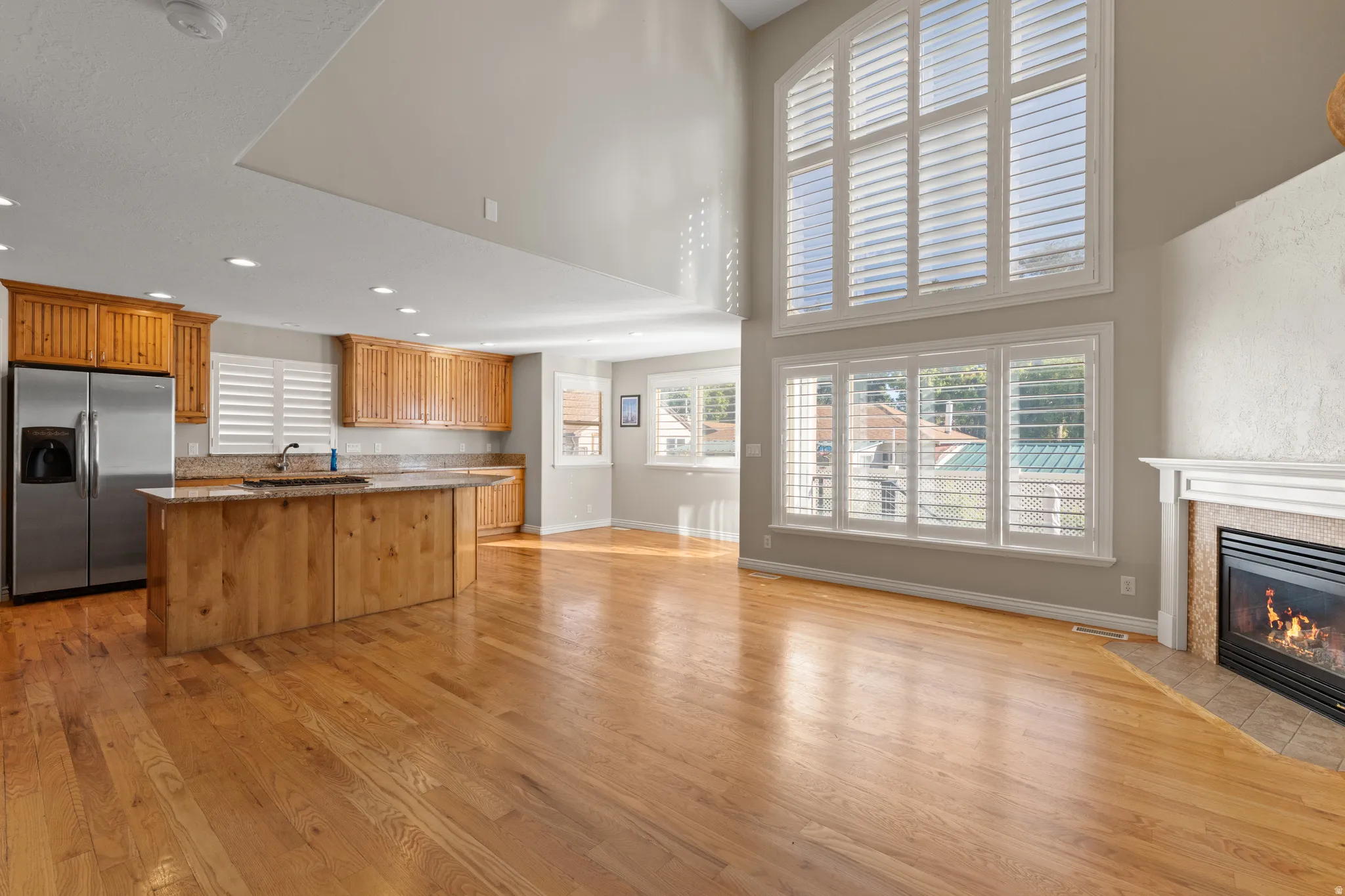 Open-concept living area with wood-finish flooring, a fireplace with a white mantel, and vaulted ceilings