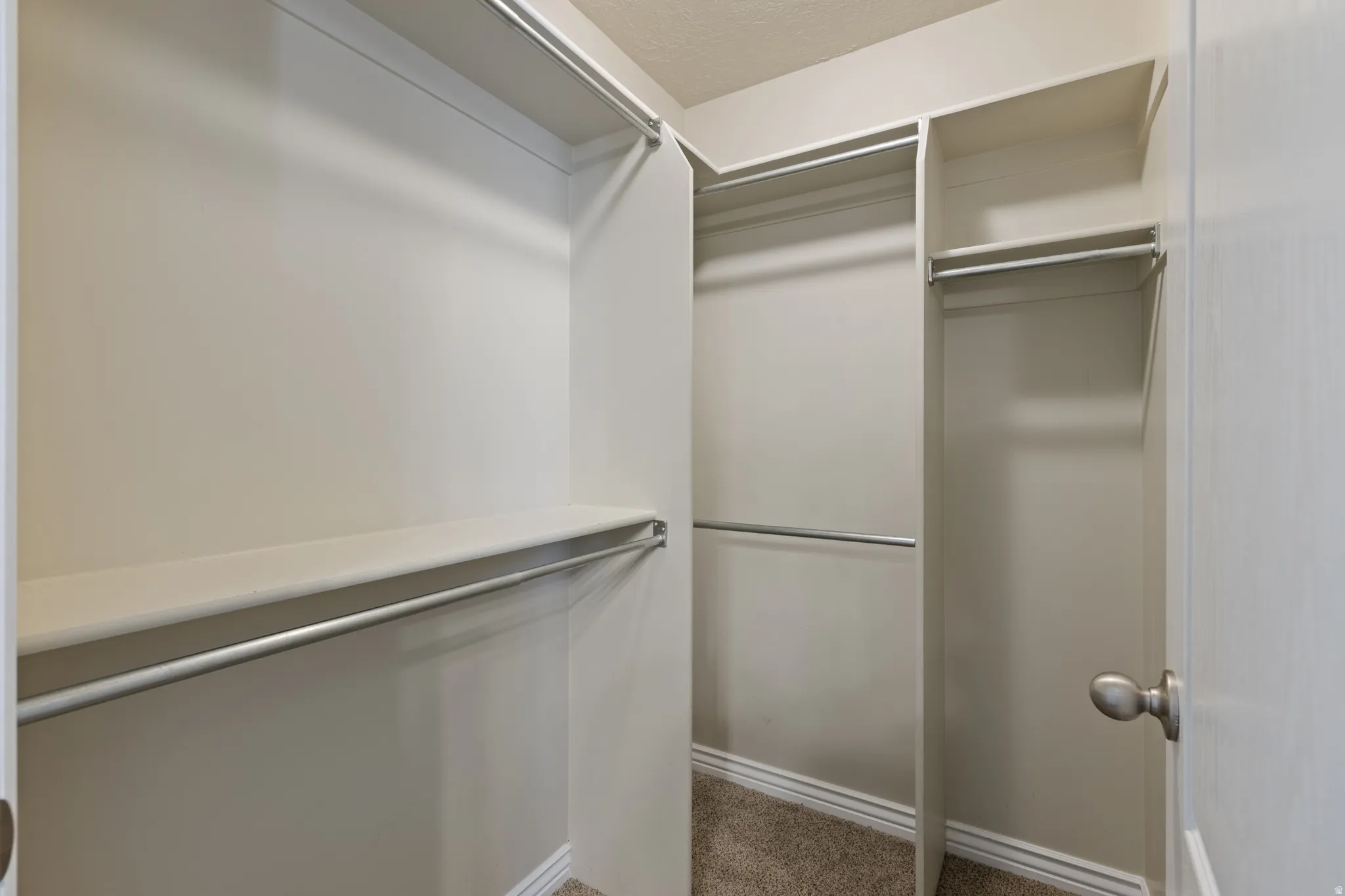 Walk-in closet with multiple shelving units and hanging rods, beige wall paint, and textured carpet flooring
