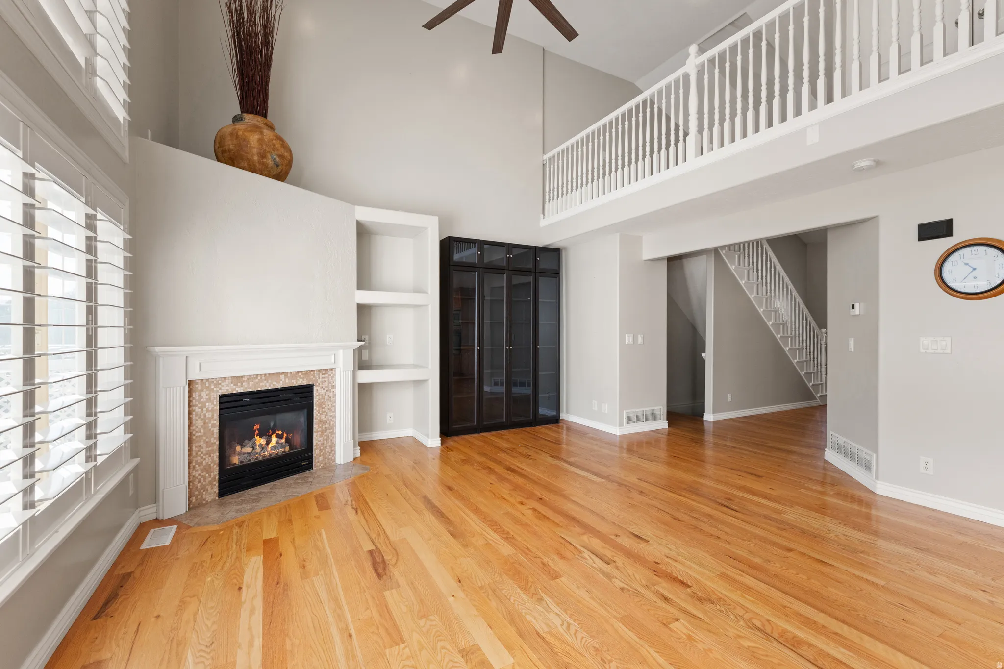 Hardwood flooring, high ceilings, fireplace with tile surround, built-in shelving, and white plantation shutters