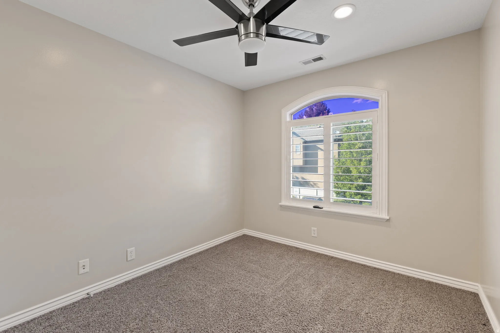 Carpeted room featuring a white arched window with plantation shutters, a ceiling fan, and recessed lighting