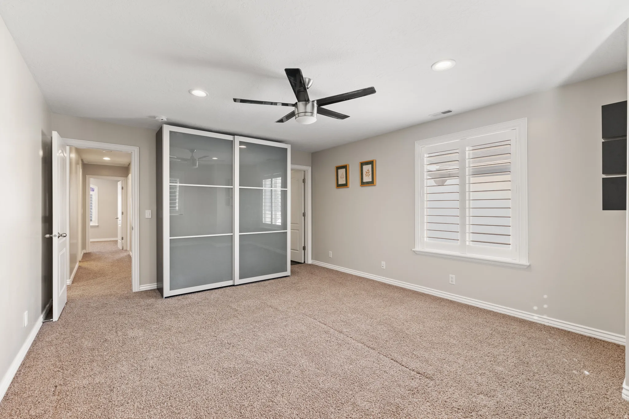 Plush carpet flooring, ceiling fan with light fixture, recessed lighting, and a window with white plantation shutters
