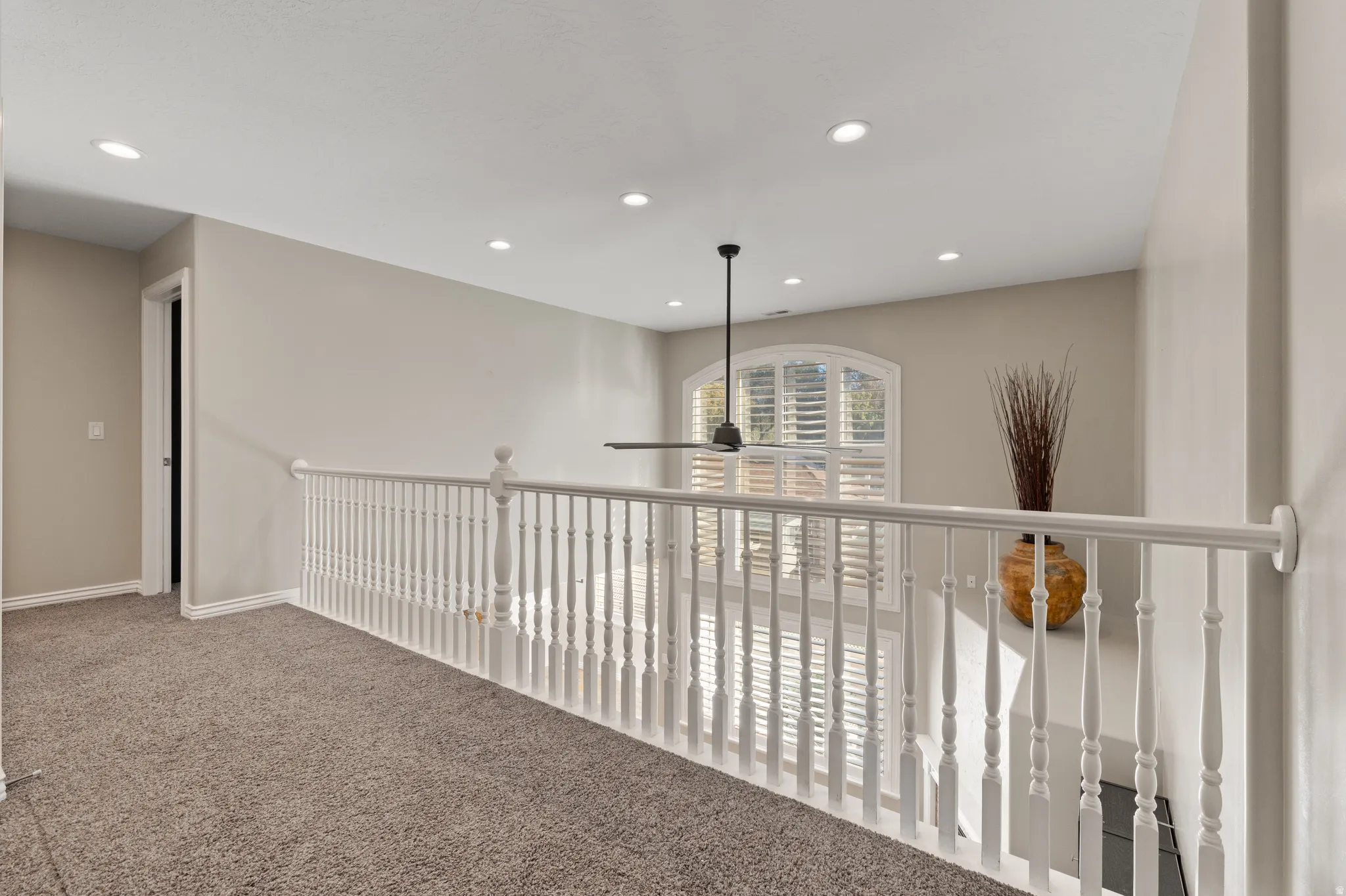 Arched window with plantation shutters, recessed lighting, ceiling fan, and white spindle railing