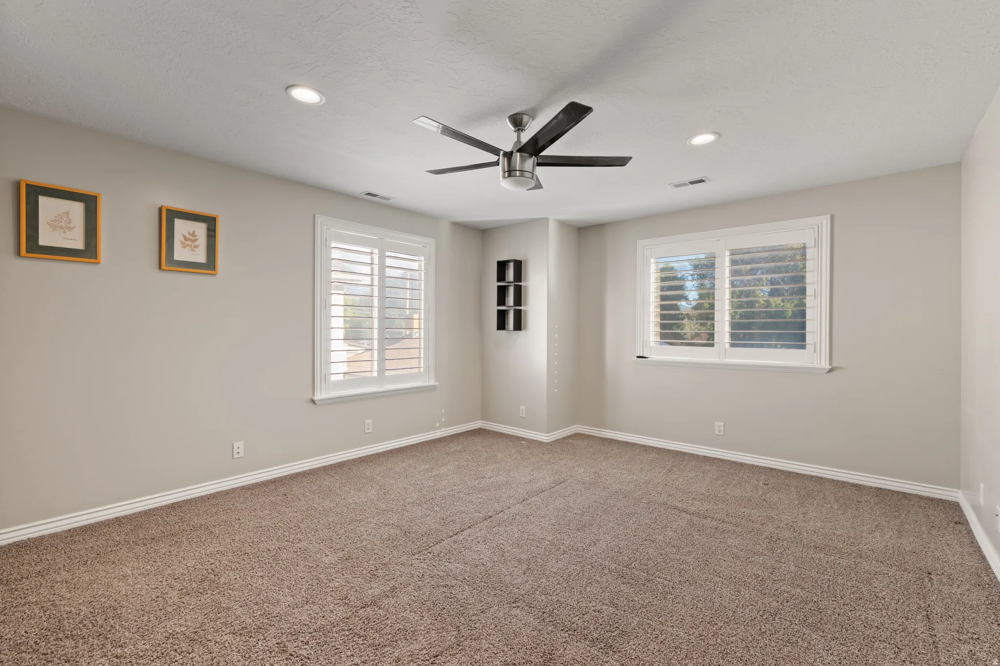 Recessed lighting, ceiling fan, two windows with plantation shutters, built-in shelving, and carpeting