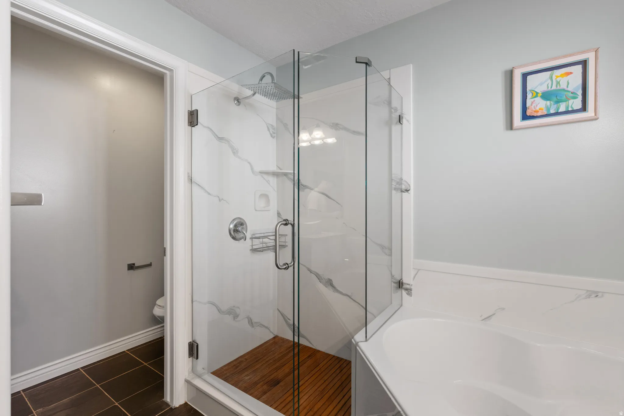 Glass-enclosed shower with a rainfall showerhead, white marble-patterned tile, and wood-finish flooring