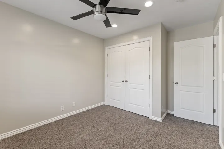 Plush carpeted flooring, two paneled closet doors, a paneled interior door, ceiling fan with integrated lighting, and recessed ceiling lights