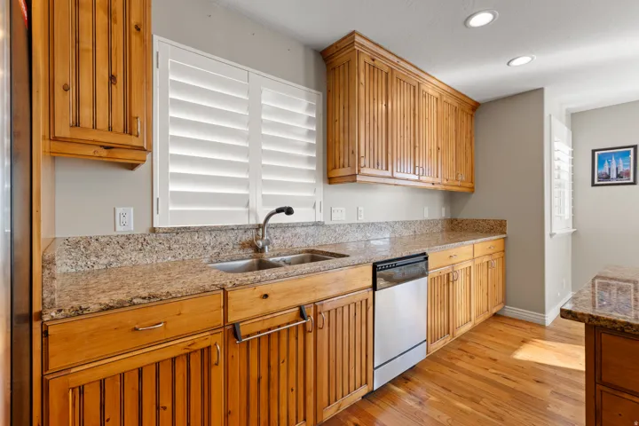 Wood-finish cabinetry, granite countertops, stainless steel dishwasher, double basin sink, and wood-finish flooring