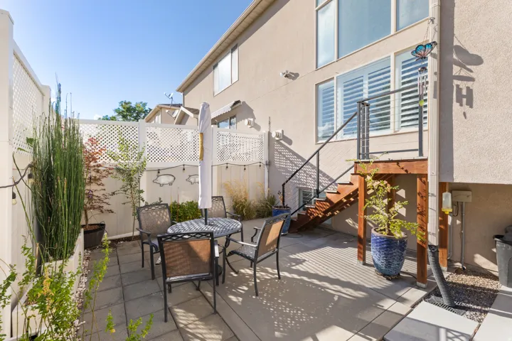 Ground-level patio with paver stones, lattice fencing, and a wood staircase with metal railings