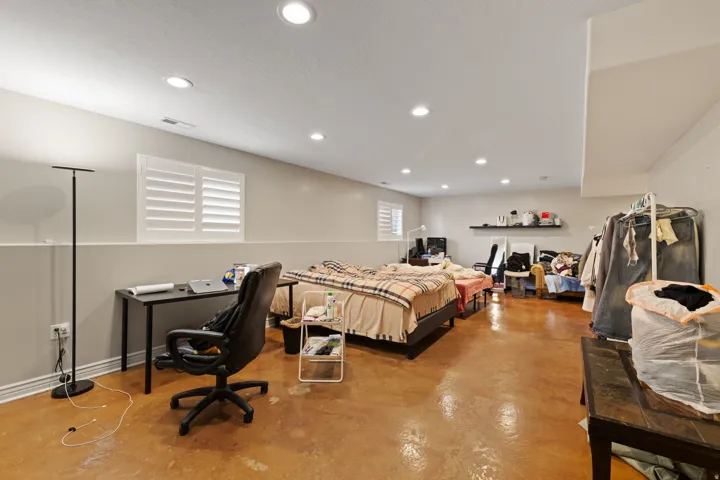 Recessed ceiling lighting illuminates the expansive room featuring two windows with white plantation shutters