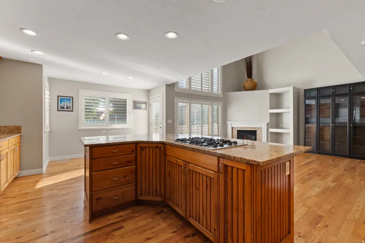 Kitchen island with integrated cooktop, wood-finish flooring, recessed lighting, and a fireplace with built-in shelving