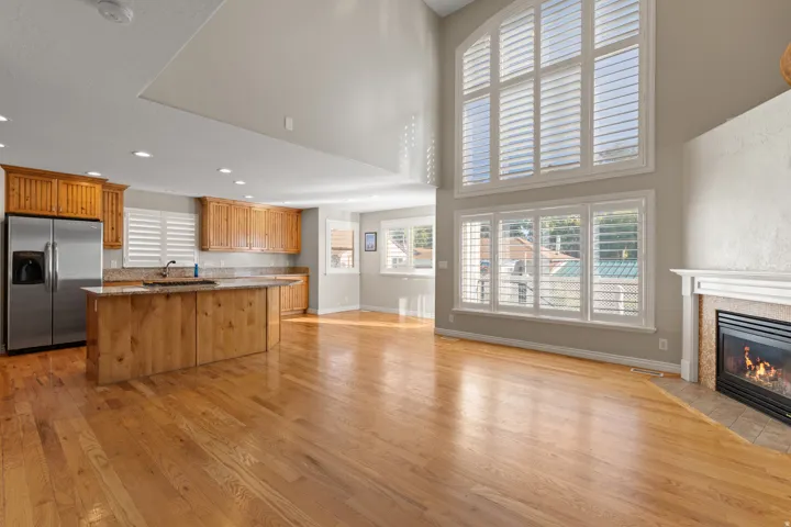 Open-concept living area with wood-finish flooring, a fireplace with a white mantel, and vaulted ceilings