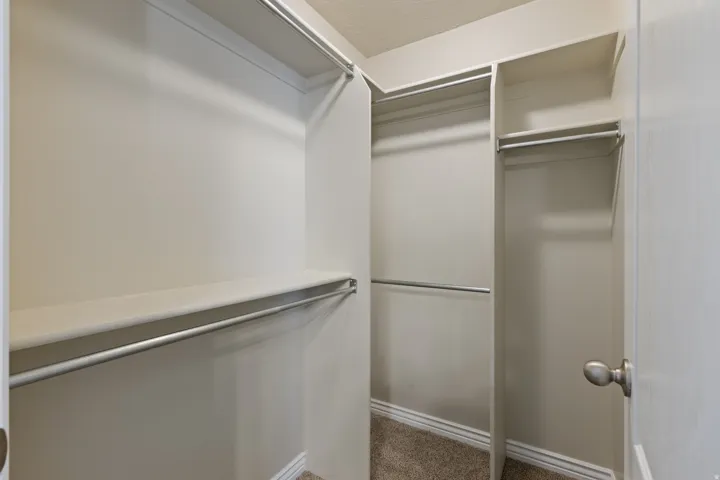 Walk-in closet with multiple shelving units and hanging rods, beige wall paint, and textured carpet flooring