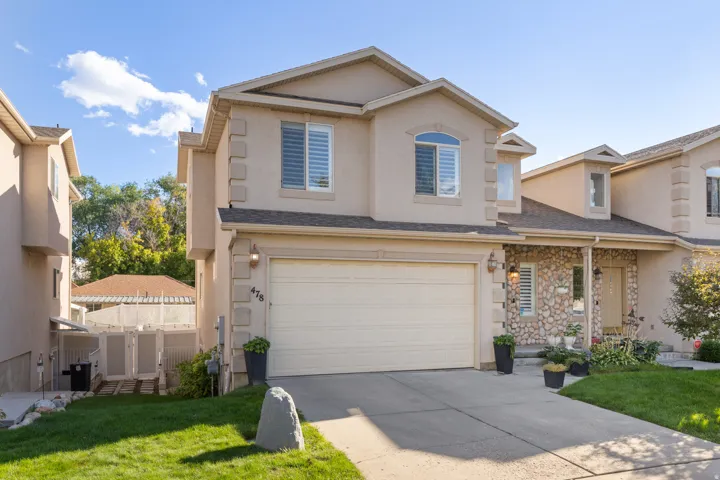 Stucco exterior with stone accents, attached garage, arched window, and front entryway with exterior lighting