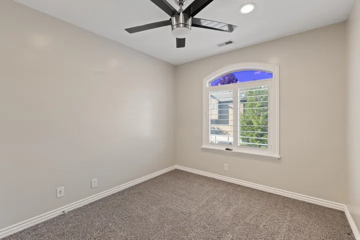 Carpeted room featuring a white arched window with plantation shutters, a ceiling fan, and recessed lighting