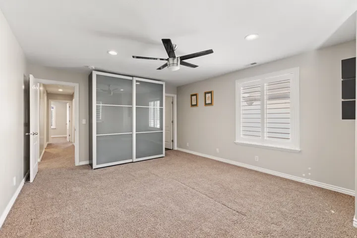 Plush carpet flooring, ceiling fan with light fixture, recessed lighting, and a window with white plantation shutters