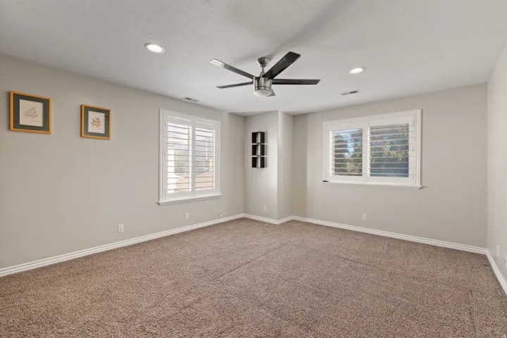 Recessed lighting, ceiling fan, two windows with plantation shutters, built-in shelving, and carpeting