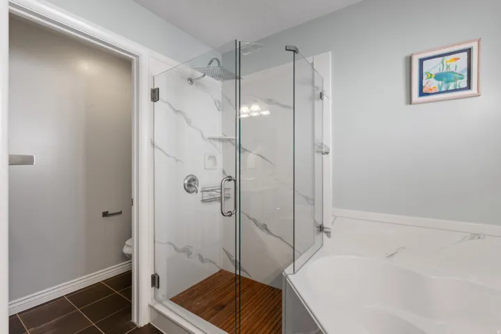 Glass-enclosed shower with a rainfall showerhead, white marble-patterned tile, and wood-finish flooring