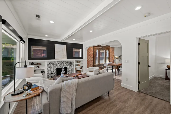 Wood-finish flooring, white shiplap ceiling, built-in shelving with patterned tile fireplace surround, and recessed lighting