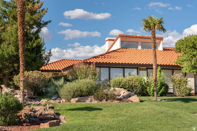 Terracotta tile roof, large windows, established landscaping, prominent palm trees, and a green lawn