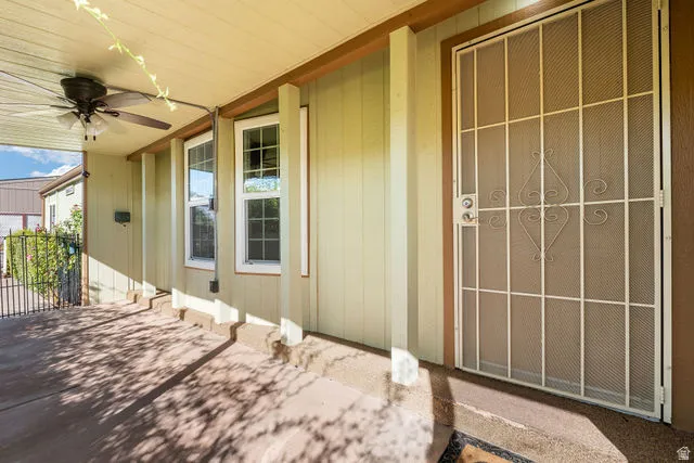 Covered concrete patio with overhead ceiling fan, white security screen door, and two double-hung windows