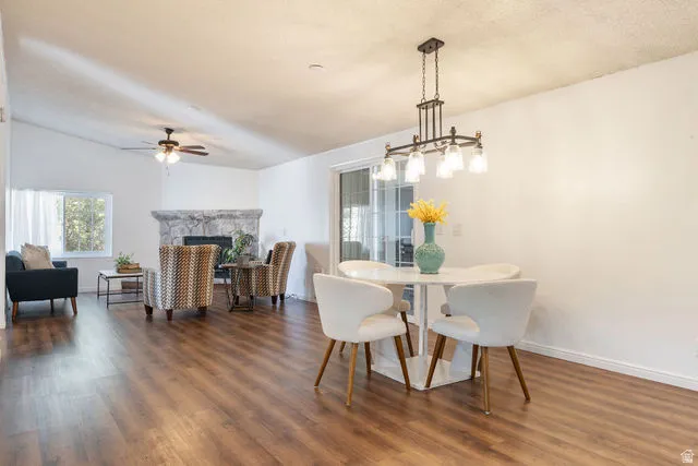 Open concept living and dining area featuring wood-finish flooring, a stone fireplace, vaulted ceilings, and a ceiling fan